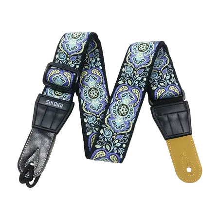 A guitar strap with a blue, purple, and green paisley pattern, featuring black leather hardware and a tan leather end cap, displayed on a white background.