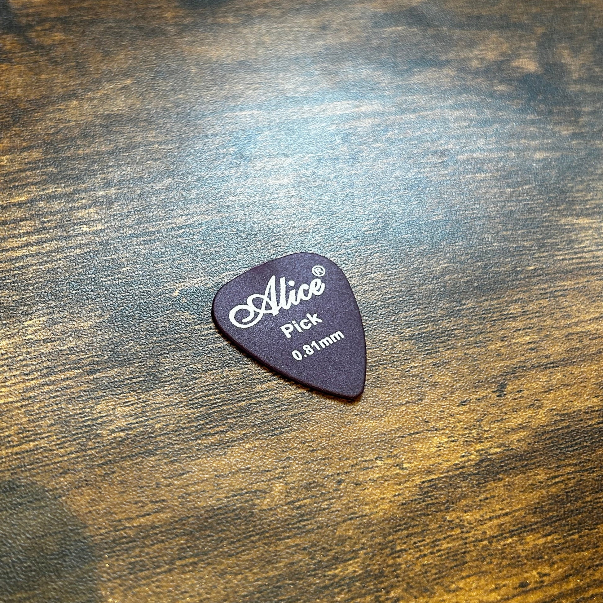 Dark Purple 0.81mm Guitar pick with 'Alice' branding on a wooden surface
