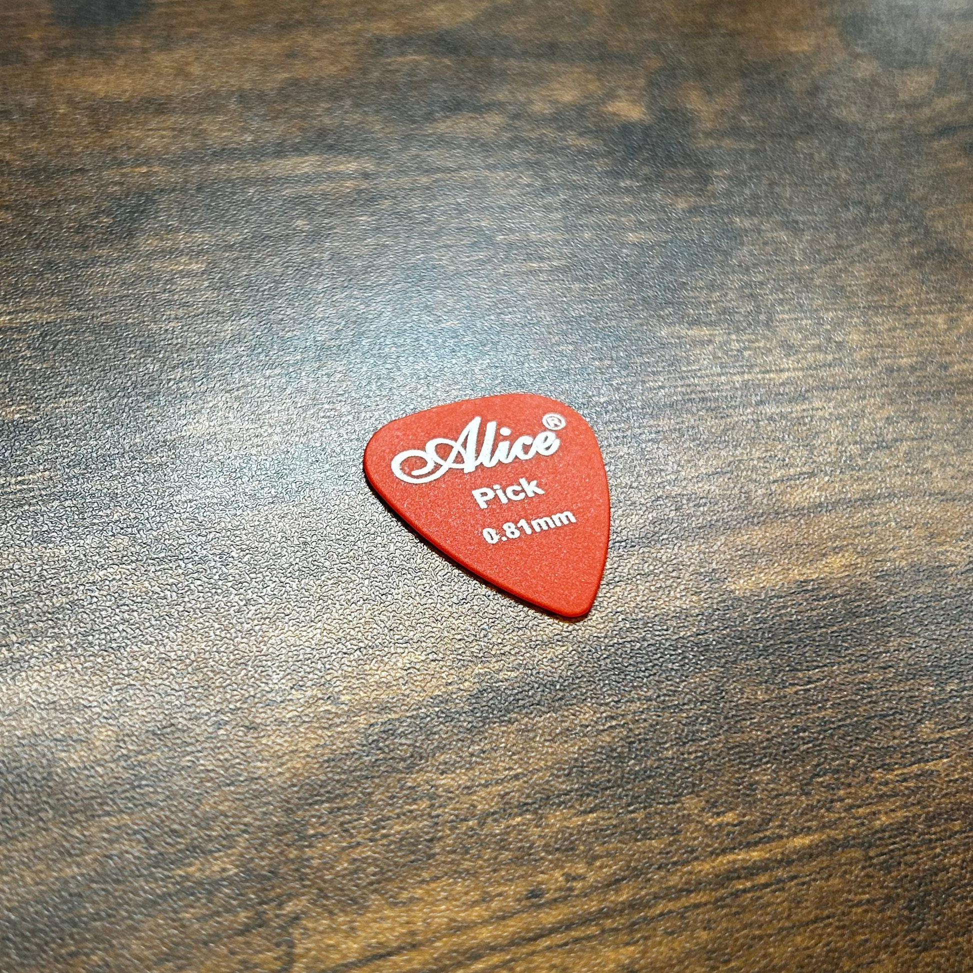 Dark Orange guitar pick with 'Alice' branding on a wooden surface