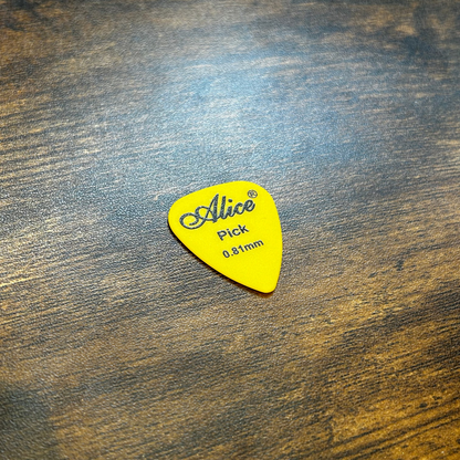 Yellow 0.81mm guitar pick with 'Alice' branding on a wooden surface