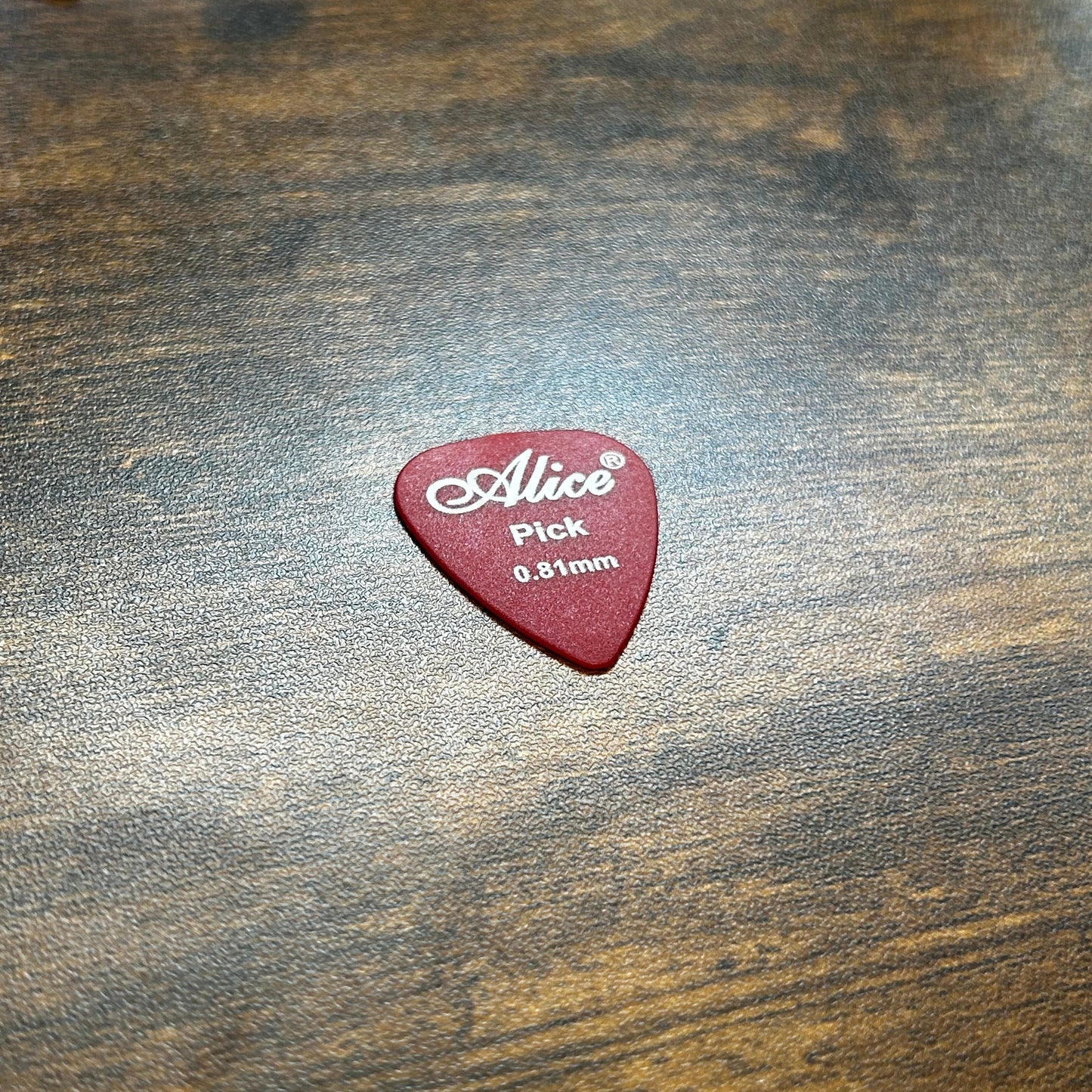 Alice 0.81mm guitar pick on a wooden desk in a bright background