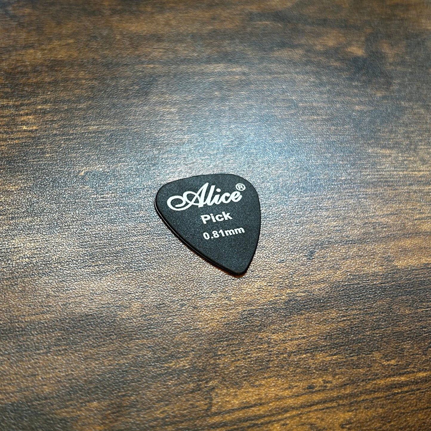 Black 0.81mm guitar pick with 'Alice' branding on a wooden surface