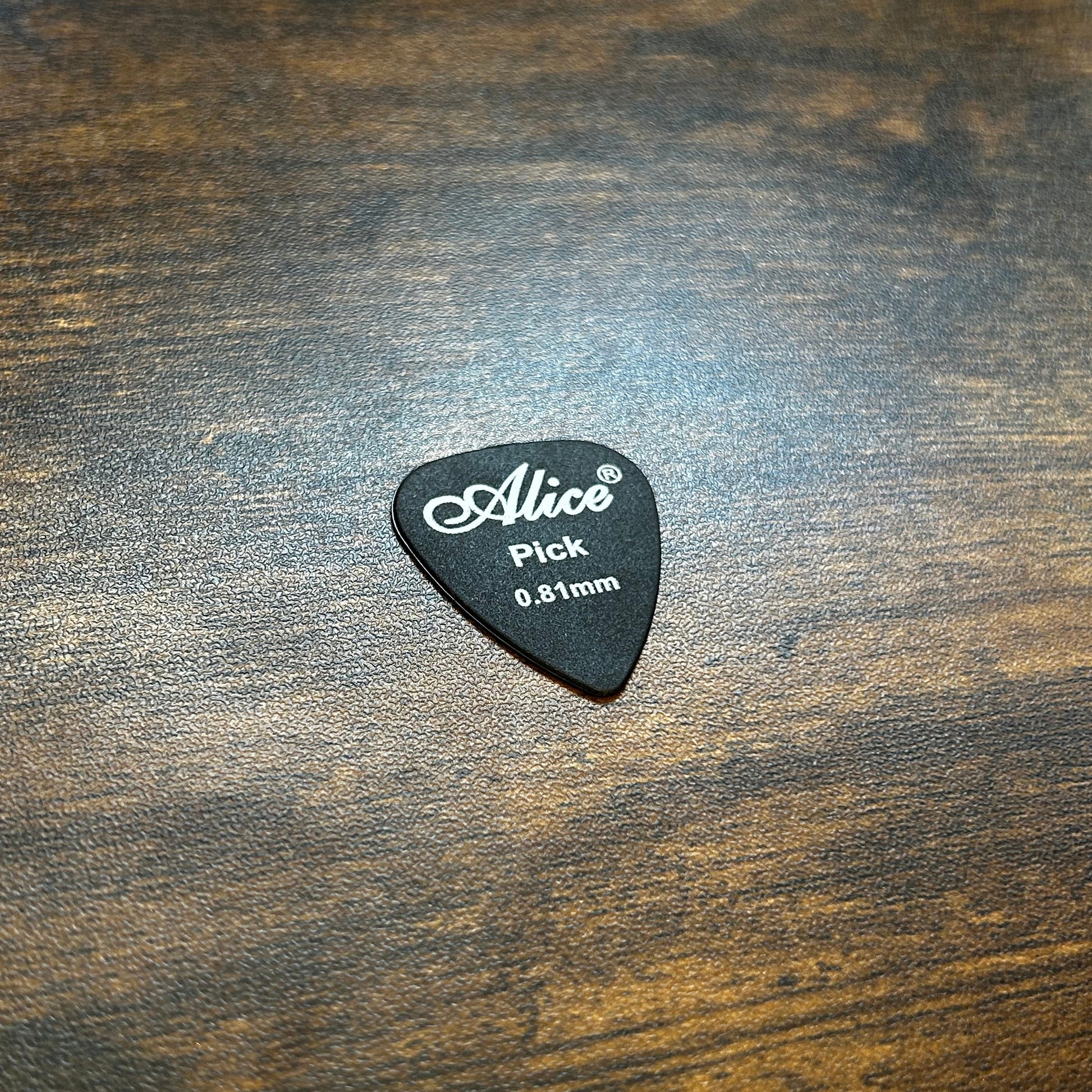 Black 0.81mm guitar pick with 'Alice' branding on a wooden surface