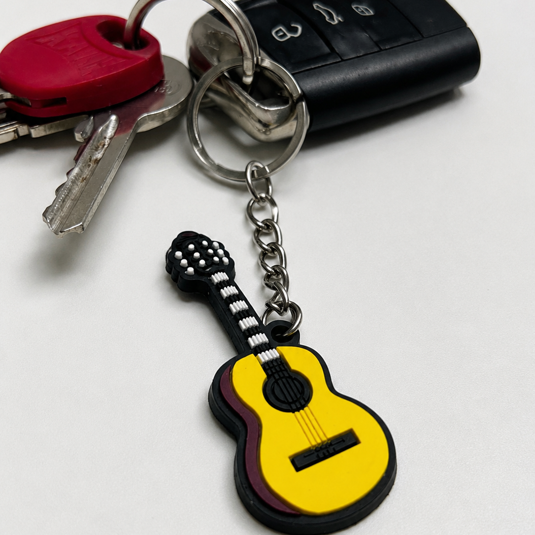 A guitar-shaped keychain charm attached to a metal keyring with keys and a black car key fob on a plain light background.