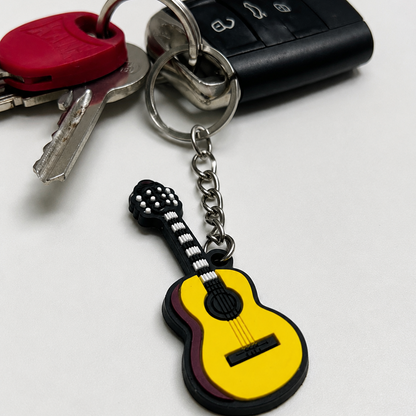 A guitar-shaped keychain charm attached to a metal keyring with keys and a black car key fob on a plain light background.