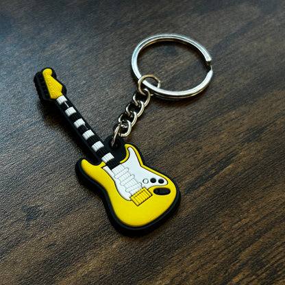 A yellow electric guitar keychain with a black and white striped neck, resting on a dark wood surface.