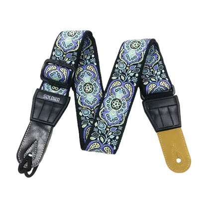 A guitar strap with a blue, purple, and green paisley pattern, featuring black leather hardware and a tan leather end cap, displayed on a white background.
