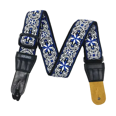 A guitar strap with a blue and white ornate scroll pattern, black leather ends, and a gold-toned metal hardware piece, displayed against a solid black background.
